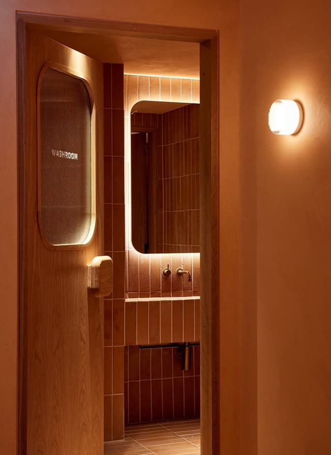 Warm-toned washroom interior at Offshore Montauk featuring wood detailing, terracotta tile, and backlit mirrors.